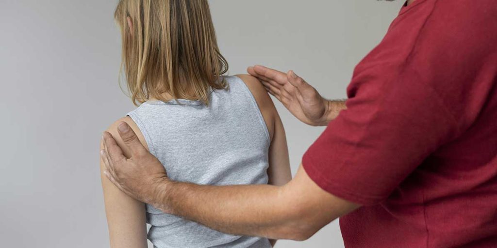 A chiropractor evaluates a patient's shoulder alignment to check for spinal misalignment symptoms and posture issues during a physical exam.