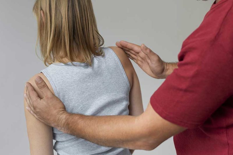 A chiropractor evaluates a patient's shoulder alignment to check for spinal misalignment symptoms and posture issues during a physical exam.